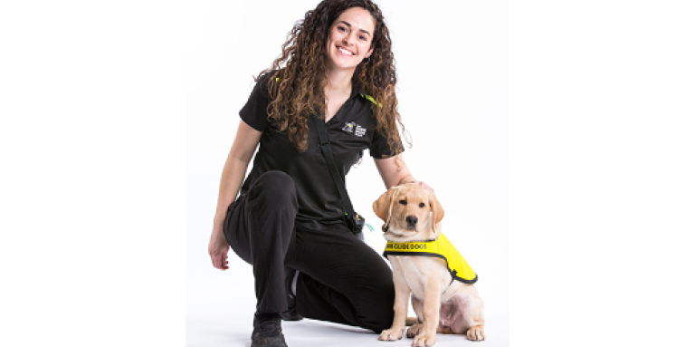CNIB Guide Dogs trainer kneels next to puppy wearing yellow vest