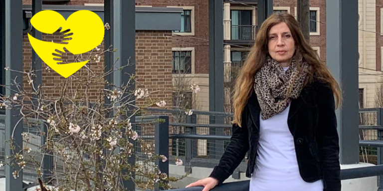 Rositsa standing outside holding a railing. A graphic of arms hugging a cartoon heart can be seen in the top left corner of the photo.
