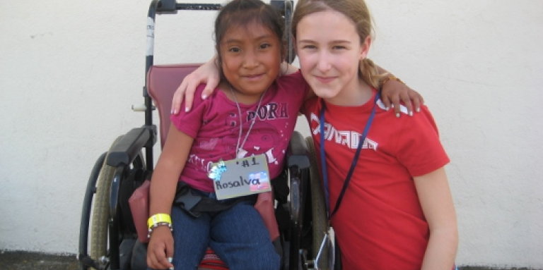 In Guatemala, a young Veronika crouches down next to a girl in a wheelchair. They have their arms around one another and pose for the photo.