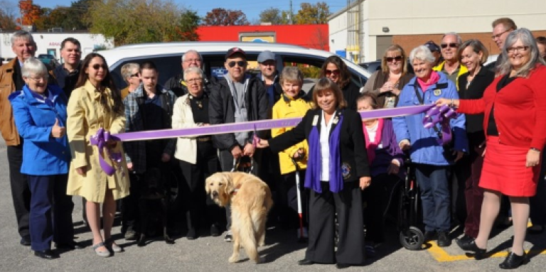 In 2015, Barb Ennis poses at a ribbon-cutting ceremony when she, as Lions District Governor for A12, purchased a brand new van to enhance client service. This van is now in service at CNIB Lake Joe!