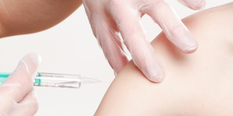 A person receiving a vaccine. A sleeveless arm is injected with a needle.