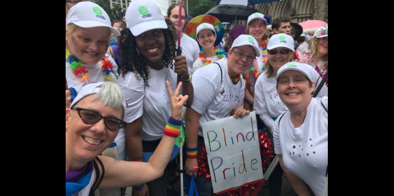 CNIB participants, staff and volunteers sporting white t-shirts, baseball caps and smiles at the Toronto Pride parade