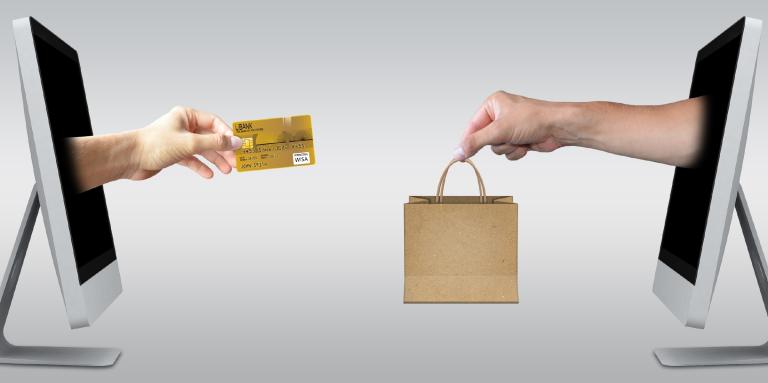 Two desktop computers with photoshopped pictures of hands coming out the monitors. On the left computer monitor, a hand is extended holding a credit card. On the right computer, a hand is extended holding a shopping bag.