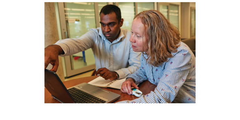 A man and a woman sitting at a desk looking a laptop screen 