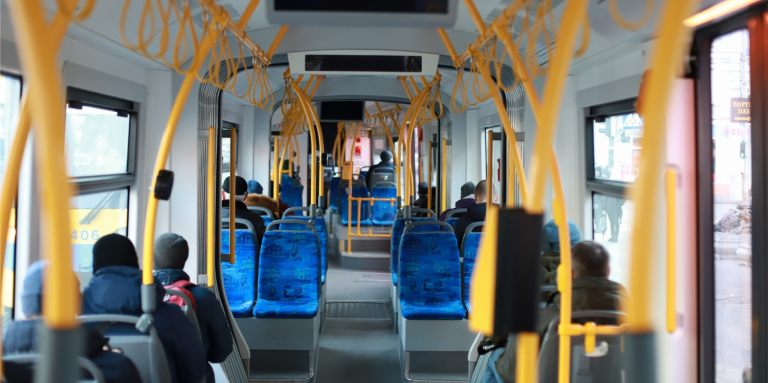The interior of a city bus with passengers seated. The image is taken from the back of the bus. 