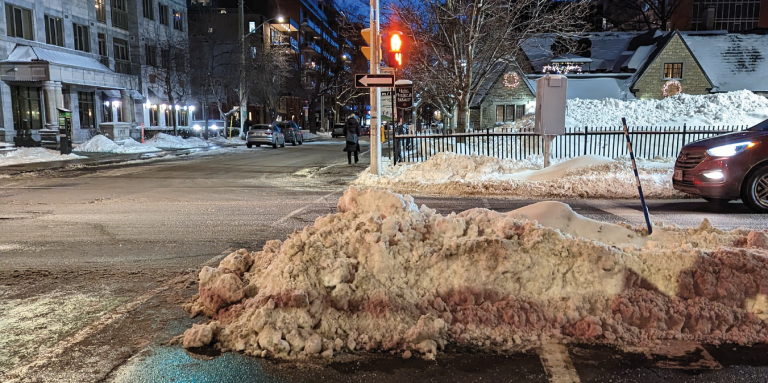 Stopped at traffic lights, a pile of improperly cleared snow blocks half of the pedestrian crosswalk.