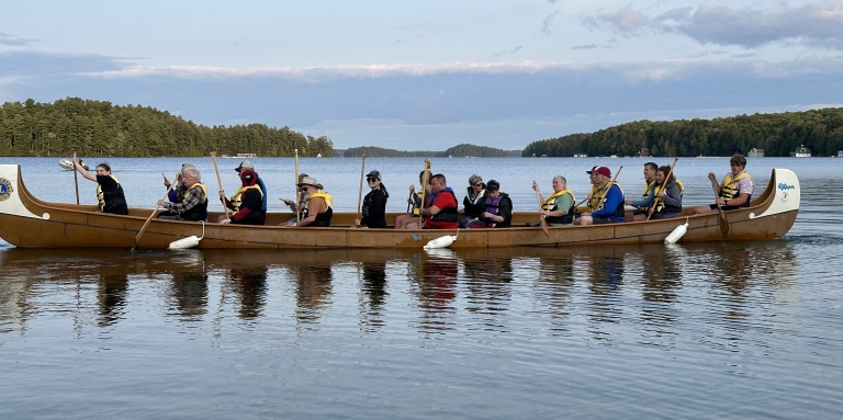 A group of 18 adult campers rowing a boat on the beautiful lake Joseph. 