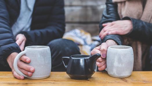 photo of two people seated at a table holding coffee mugs.