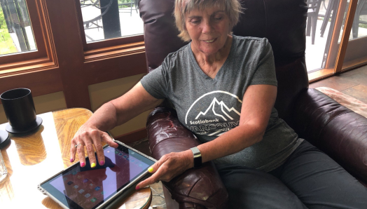 Marilyn est assise sur une chaise et tape sur un iPad. L'appareil est posé sur une table basse à droite de la chaise