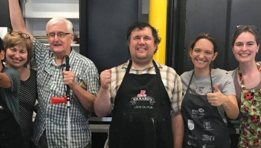 Un groupe de 7 personnes avec le pouce en l'air dans la cuisine du Hub portant des tabliers