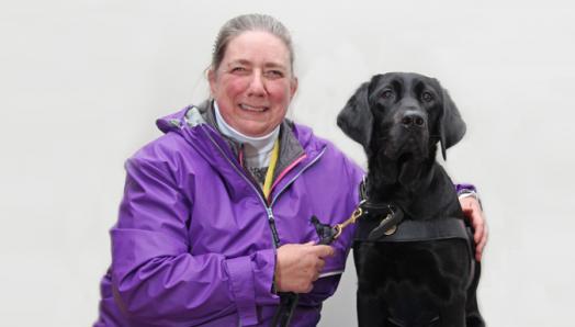 Une femme portant une veste mauve et son chien de race croisée Labrador noir-Golden Retriever chien-guide.