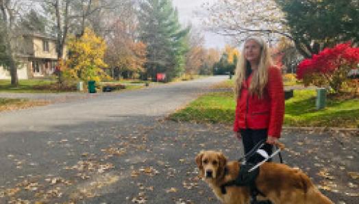 Diane Bergeron marche avec son chien-guide, Carla. Carla porte un harnais et se tient à sa gauche.