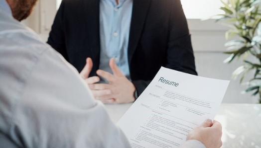 A job interview. An employer holds a resume. In front of him is someone being interviewed.