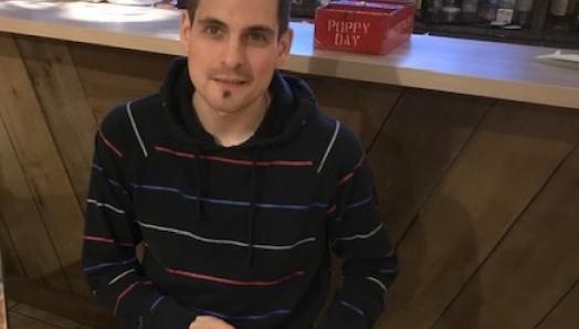 Ryan Hooey assis dans un restaurant, tenant une pompe à insuline et souriant pour la caméra.