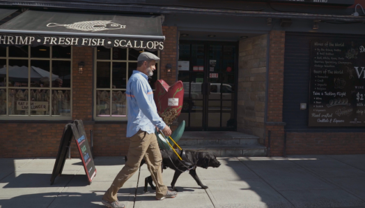 Lawrence and his guide dog Lewis, walking down the sidewalk on a sunny day.