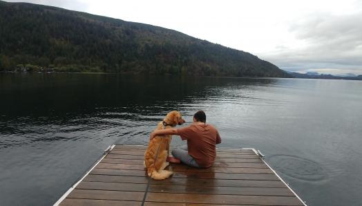 Landon et Ruggles, un Golden Retriever, assis sur un quai surplombant un lac; Landon passe son bras sur le dos de Ruggles qui regarde son jeune maître