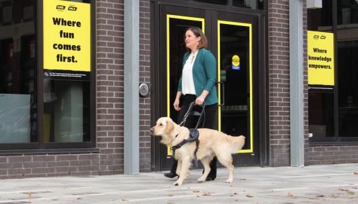 Photo of Erin & Winston walking along a sidewalk in front of a CNIB Foundation building. 