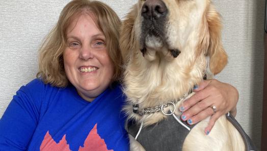 Chris, wearing a blue shirt with a red maple leaf on the front of it, sitting on the floor next to Cody while smiling for the camera.