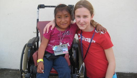 Au Guatemala, une jeune Veronika s'accroupit à côté d'une jeune fille en fauteuil roulant. Elles se tiennent par le bras et posent pour la photo. 