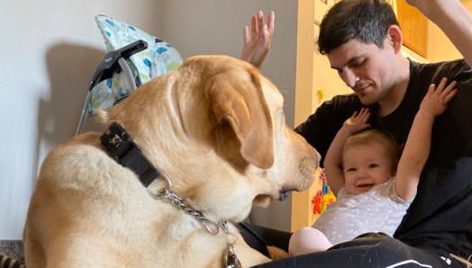 Ryan et sa fille Abigail, assis par terre jouant avec Joe, un chien-guide d’INCA.