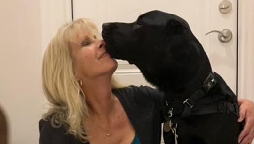 Karen sitting on her steps getting a kiss on the face from Healey, her CNIB Guide Dog. 