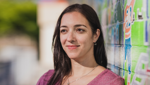 Une photo-portrait de Stefanie Volpe à côté d'un mur rempli de graffitis colorés. 