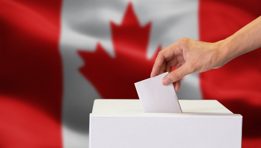 A hand dropping a ballot into a box; the Canadian flag in the background.