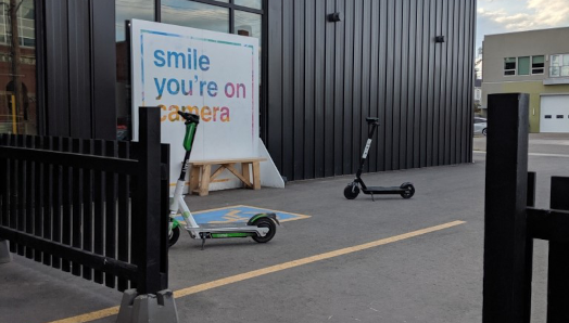 Deux trottinettes électriques disposées côte à côte sur un trottoir à l'extérieur d'un commerce à Edmonton.