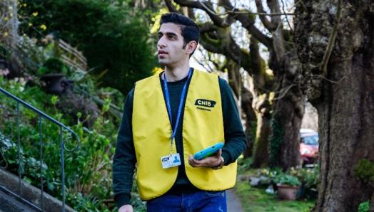 CNIB Fundraiser in a yellow vest with an ID badge and tablet