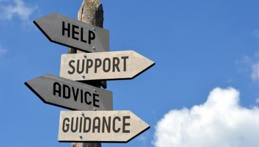 Sign post with the words "help", "support", "advice", "guidance: on wooden arrow signs pointing in different directions with a blue sky in the background.